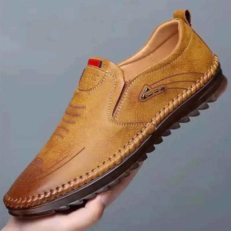 Brown leather shoe held by a hand against a gray background